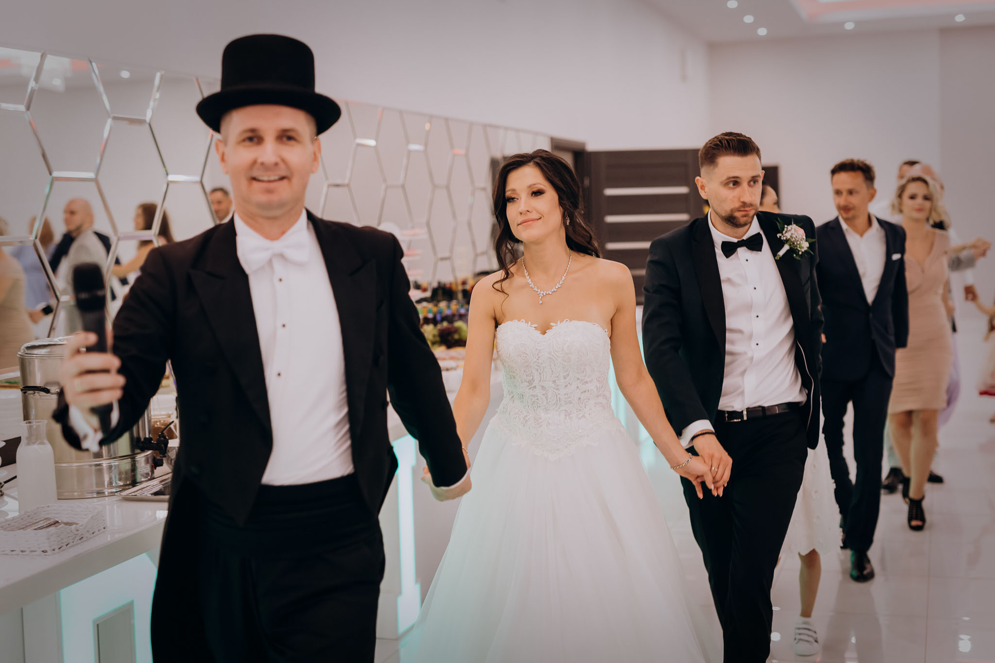 Panna Młoda i Pan Młody wchodzą razem z wodzirejem polonezem na przyjęcie weselne