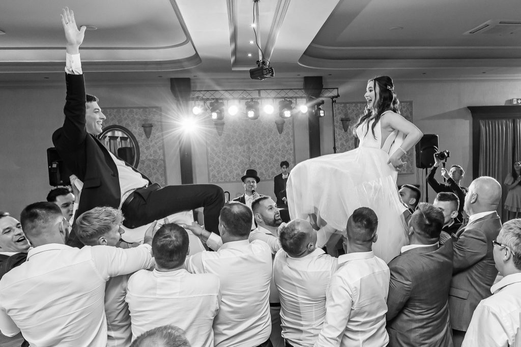 Państwo Młodzi podnoszeni są na krzesłach. DJ czuwa, aby wyciszyć muzykę w danej chwili, żeby bardziej były słyszane emocje.